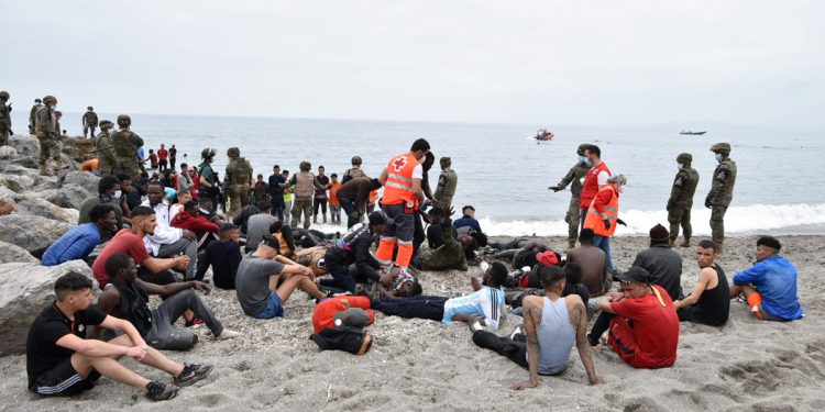 Red Cross members assist migrants who arrived swimming at the Spanish enclave of Ceuta as Spanish soldiers and Guardia Civil members stand guard on May 18, 2021 in Ceuta. - Spain has returned to Morocco nearly half of the 6,000 migrants who entered its Ceuta enclave, as hundreds more tried to enter its other north African territory. (Photo by Antonio Sempere / AFP)
